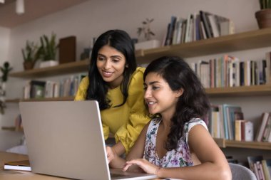 Modern ofiste dizüstü bilgisayar kullanan iki çekici Hintli iş arkadaşı, cihaz ekranına bakın, yeni platformu gözden geçirin, ortak proje için fikir üretin, veri veya raporları analiz edin, pazarlama stratejisini tartışın