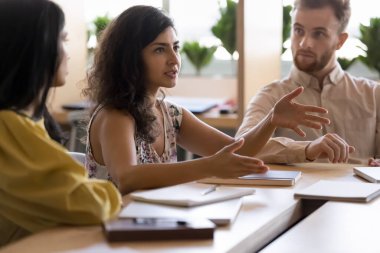 Ofiste grup toplantısında konuşan yetenekli Hintli kadın, çeşitli meslektaşlar, personel üyeleri ile konferans masasında oturuyor, açıklama yapıyor, paylaşım noktası kendinden emin görünüyor. Liderlik, fikir