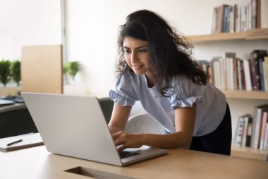 Genç Hintli bayan öğrenci ya da ofis çalışanı, çalışma masasına dayanan ve belgeyi düzenleyen modern dizüstü bilgisayarla İnternet 'te çalışıyor ya da çalışıyor. Modern çalışma ortamında iş e-postalarına cevap verirken odaklanmış görünüyor.