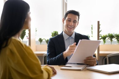 Gülümseyen İspanyol işadamı, yazılı bilgileri gözden geçiren, geri bildirim sağlayan, iş görüşmesi yapan ya da iş konularını kadın meslektaşıyla ya da iş başvurusunda bulunan kişiyle tartışan bir yığın kağıt tutuyor.