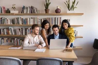 Dört genç, yetenekli iş arkadaşı konuşuyor, modern dizüstü bilgisayarla beyin fırtınası yapıyor, brifing sırasında işbirliği yapıyorlar. Yeni Yapay Zeka programını, kurumsal yazılımı veya ortak projeyi inceleyen personelin ekip çalışması