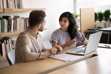 İki çok uluslu iş arkadaşı projeyle ilgili tartışmayı yürütürken ortak çalışma ofisinde dizüstü bilgisayar kullanarak bir araya geldiler. Fikir sunan, konuyu açıklığa kavuşturan Hintli kadın takım üyeleriyle brifing sırasında yaratıcı fikirleri paylaşıyor.