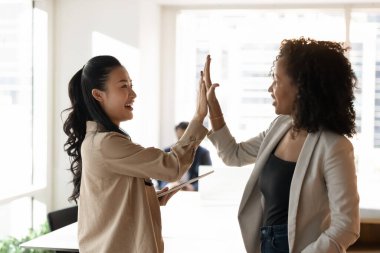 İşbirliği ve birlik. Heyecanlı genç profesyoneller çok ırklı kadın iş arkadaşları beşlik çakıyor iş başarısını kutluyorlar ortaklık çalışmaları arkadaşça motivasyon desteği veriyor