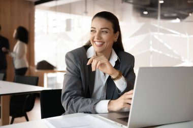 Yaratıcı düşünme ve görselleştirme. Neşeli genç iş kadını iş yerinde dizüstü bilgisayarının başında oturur rüya gibi bir gülümsemeyle başka tarafa bakar yeni bir çözüm yaratır gelecekteki hedeflere yansıtır dikkatli mola alır. Boşluğu kopyala