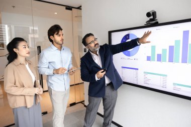 Şirket eğitimi ve aktif öğrenme. Olgun iş adamı akıl hocası dijital kuruldaki çeşitli genç meslektaşlarına iş verileri grafikleriyle proje stratejisini açıklıyor ve büyüme olanaklarını gösteriyor.