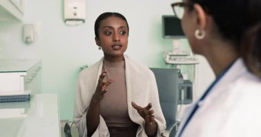 Genç ve güzel Afrikalı hasta kadın klinikteki doktora danışmanlık yapıyor, çalışma masasında oturuyor, tıp uzmanıyla konuşuyor, şikayetlerde bulunuyor, tedaviyi anlatıyor, terapiyi anlatıyor.