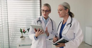 50 'li yaşlardaki kadın doktor günlüğü ya da kişisel organizatör genç bayan meslektaşla konuşuyor, tabletteki anesteziyi gözden geçiriyor, tedavi planını tartışıyor, klinikteki tıp konseyini meşgul ediyor.