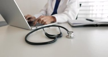 Dizüstü bilgisayarda çalışan kadın doktor görüşü, masadaki steteskopa odaklan. Modern teknolojiyi kullanan, iş arkadaşlarıyla iletişim kuran, tedavi planını hastalarla paylaşan bir tıp çalışanı.
