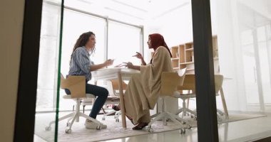 Pazarlık eden iki profesyonel çok kültürlü iş kadını konferans masasında oturmuş, ayrıntılı sözleşme görüşmeleri, şartları gözden geçirme veya kararlaştırılmış noktaları belgeleme konularında yer alıyorlar. Karar verme, iş, anlaşma