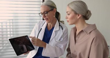 Paltolu kadın travmatolog kadın hasta için tablet ekranda gösterilen röntgen görüntüsü tarama sonuçlarını açıklıyor, teşhis, yaralanma ve tedavi planını tanımlıyor.