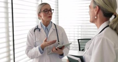 Beyaz üniformalı genç bir kadın terapist olgun, deneyimli bir bayan meslektaşla konuşuyor, el sıkışıyor, klinikte tartışmaları başarıyla sonuçlandırıyor. Saygı, etkili işbirliği