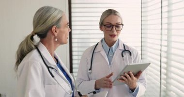 Klinikte konuşma yapan iki doktor, hasta vakaları, teşhis, tedavi seçenekleri, test sonuçları veya iş akışı koordinasyonu hakkında fikir alışverişinde bulunarak, protokolleri güncellemeleri ve ilaç planlarını tartışırlar.