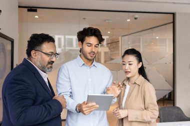 İş diyaloglarında dijital veriler. Muhtelif çok ırklı iş adamları grubu ofiste duruyor ve çevrimiçi belge üzerinde tartışmak için tablet bilgisayar kullanıyor. Pazarlama planı için fikirler yaratıyor ürün tanıtım stratejisi geliştiriyor.