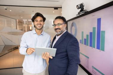 Akıl hocalığı ve işbirliği. İki iş adamından oluşan bir ekip genç stajyer orta yaşlı akıl hocası modern ofiste durup mutlu bir gülümsemeyle kameraya bakıyorlar. Dijital PC 'yi başarılı bir ortak proje araştırması yapmaktan gurur duyuyor.