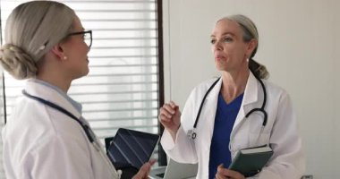 Olgun ve genç kadın doktorlar klinikte konuşuyor, el sıkışıyor, tıp konseyini sonuçlandırıyor, fikir alışverişinde bulunuyor. Cerrahi hazırlık koordinasyonu, hasta tanısı doğrulama, tedavi planı anlaşması