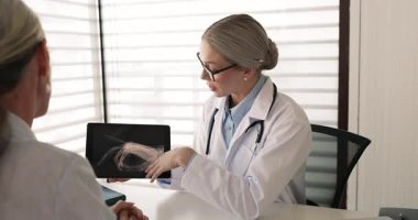 Travmatolojist ekranda gösterilen röntgen görüntülerinde tablet ve noktalar tutuyor, kol kırığı veya çıkığı tedavi planını açıklıyor, tanı paylaşımı, ileri terapi ve yaşlı hastaya rehabilitasyon