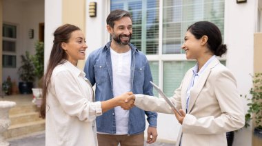 Eşler ve emlakçılar el sıkışıyor, dışarıda duruyorlar. Ev sahibi olma ya da mülk satma hayalleri kuran çift başarılı bir emlak alışverişi yapıyor, anlaşmayı imzaladığı için tebrik ediliyor.