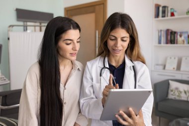 Pozitif kadın İspanyol doktor, tabletten kadına tıbbi test sonuçları gösteriyor, hastaya danışmak için cihaz kullanıyor, reçeteyi, tedaviyi, teşhisi, elektronik kontrol raporunu,