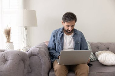 Kucağında dizüstü bilgisayarla koltukta oturan, ekrana ve daktiloya bakan, işle ilgili işlerle meşgul olan, internete bakan, hafta sonları iş ya da kişisel e-postalarına cevap veren odaklanmış bir adam.