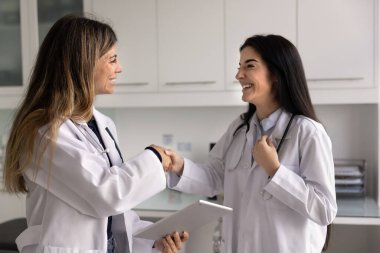 Klinikte el sıkışan iki mutlu Latin doktor kadın. Neşeli genç İspanyol tıp uzmanının iş arkadaşına el sıkışması, yardım, destek, tavsiye, takım çalışması için teşekkür etmesi.