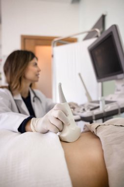 Sonografi doktoru hastanın karnına ultrason cihazı takıyor, karın organlarını inceliyor, monitöre bakıyor, modern tıbbi teknolojiyi ve ekipmanları hasta kontrolü için kullanıyor. Dikey çekim