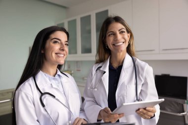 Klinikte yan yana duran iki mutlu kadın doktor, bakışlarını kaçırıyorlar, gülümsüyorlar, profesyonel kurumsal desteğin tadını çıkarıyorlar, takım çalışması, tablet tutuyorlar. Sağlık çalışanları samimi bir portre yaptılar.