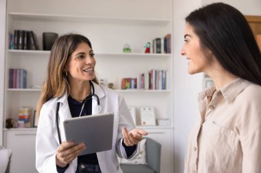 Mutlu kadın doktor hasta kadınla konuşuyor, elinde tablet bilgisayarla konuşuyor, konuşuyor ve gülümsüyor, tıbbi kanepede oturuyor, hasta kadınla terapi, iyileşme ve başarılı tedavi hakkında konuşuyor.