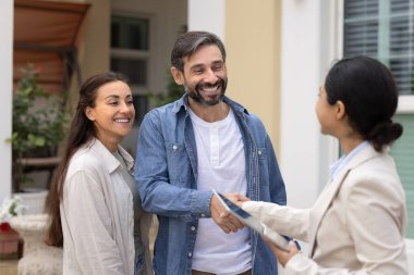 Güzel Latin çift emlakçıyı selamlıyor, emlak işlemlerine başlıyor modern kır evinin verandasında duruyor, gülümsüyor, müzakere sonuçlarından memnun oluyor, profesyonel hizmetler alıyor.