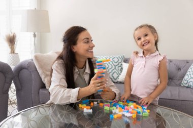 Genç, sevgi dolu anne ve 3 'lü yaşlarındaki kızı oturma odasındaki masada oturan renkli yapı taşlarıyla oyun oynuyorlar. Beraberlik, yaratıcılık, çocuklarla gelişim oyunları