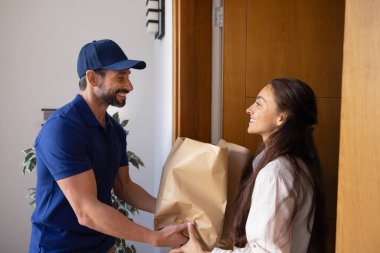 Kurye, içinde yiyecek, market veya perakende ürünleri olan iki kese kağıdını ev verandasında yan yana durarak tatmin olmuş kadın müşteriye verir. Düzenli teslimat hizmetleri, kişisel kolaylık, erişilebilirlik