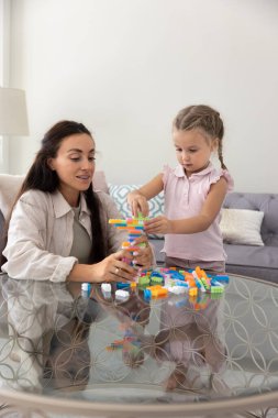 Anne ve küçük kızı oturma odasındaki renkli bloklarla oyun kulesi dizme oyunu oynuyorlar. Anaokulu çocuklarıyla evde eğitim, gelişim aktiviteleri, konsantrasyon.