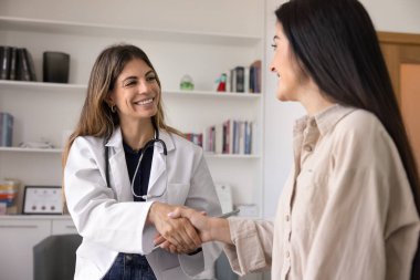 Neşeli İspanyol genç kadın ve doktor danışma toplantısından sonra klinikte el sıkışıyor. Pratisyen kadın hastaya iyileşmeyi diliyor, dişlek bir gülümsemeyle el sıkışıyor.