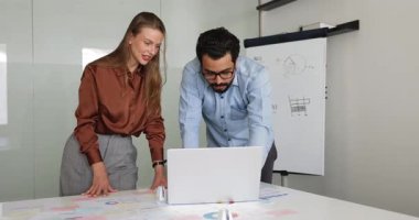 Çeşitli genç pozitif iş arkadaşları birlikte kağıt raporları üzerinde dizüstü bilgisayar kullanıyorlar, İnternet başlangıç pazarlama stratejisini analiz ediyorlar, ofis toplantılarında çevrimiçi içeriği izliyorlar ve tartışıyorlar.