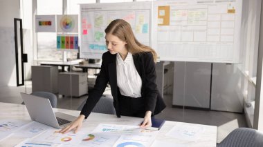 Proje analizleri, kağıt satış raporları, pazarlama araştırma sonuçları büyük çalışma tablosu, kriterler, sayım maliyetleri üzerinde çalışan odaklanmış genç ürün yöneticisi kız