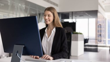 Mutlu genç 20 'li yaşlarda iş kadını ofis çalışma alanında bilgisayar başında çalışıyor, tek başına, klavyede büyük ekranda yazı yazıyor, gülümsüyor, gülüyor. Kopyalama alanı ile afiş görüntüsü