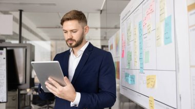 Ciddi genç şirket CEO 'su resmi takım elbisesiyle sosyal medyada dijital tablet üzerinde geziniyor, alet kullanıyor, iş iletişimi için modern elektronik teknoloji, proje planı. Pankart