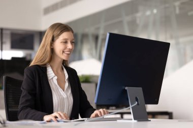 Neşeli, pozitif, başarılı, bilgisayar başında çalışan, gülümseyen, masaüstü monitörünü kullanan, klavyede yazan, online iletişim için bilgisayardaki iş uygulamasını kullanan profesyonel kız.