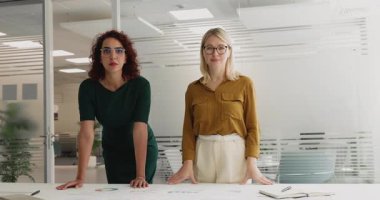 İki kadının portresi, proje yöneticileri ya da koordinatörler masanın arkasında ellerinde çizelgeler ve şemalarla görsel verileri gösteriyorlar, tartışma, iş stratejisi veya planlama ile meşguller.