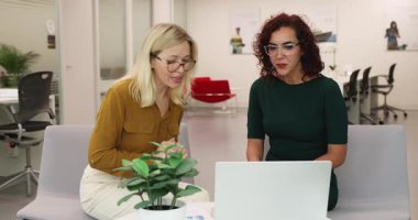 Modern çalışma ofisinde oturan iki çekici profesyonel kadın, yeni kurumsal yazılımları tartışıyor, fikir alışverişinde bulunuyor, çözüm veya fikir alışverişinde bulunuyor, ortak online sunum veya proje üzerinde çalışıyor