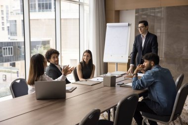Özenli erkek lider sunucu resmi takım elbise giyer ofis yönetim kurulunda çeşitli etnik çeşitlilikte çalışanların olduğu bir toplantı düzenler kadın çalışanın fikir önerisini dinler.