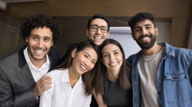 Gayri resmi ortam. Çeşitli etnik çeşitlilikteki beşinci grup fotoğrafçısı gülümseyen genç insanlar. Öğrenci bürosu çalışanları web kamerasına sarılıp birlikte video görüşmesi yapıyorlar.