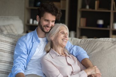 Oğlunun şefkatli kollarında. Mutlu yaşlı kadın anne büyükanne kanepeye uzan gülümseyen genç adama yaslan yetişkin torun sevgili yetişkin çocuğun elini okşa duygusal destek hisset.