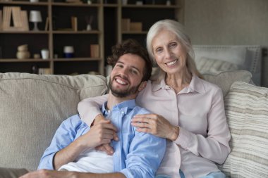 Yetişkin bir çocuğun bile anne şefkatine ihtiyacı vardır. Sevgi dolu nesiller arası aile portresi. Sevgi dolu son sınıf anne, büyük anne kucak, mutlu yetişkin torun. Kanepede uzanmış kameraya bakarak gülümsüyor.