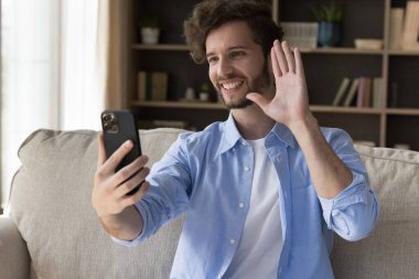 Dijital iletişim. Olumlu gülümseyen milenyum hipster çocuğu kanepede oturup akıllı telefonlu web kamerasına merhaba diyor arkadaşa video görüşmesi yapıyor sosyal medya blogu için komik selfie çekimleri yapıyor.