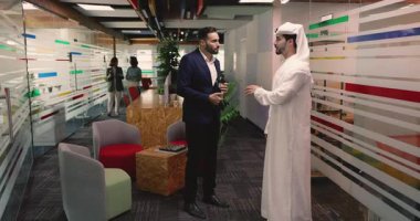 Modern iş yerindeki çok uluslu takım üyelerinin rahat çalışma salonunda iş tatili sırasında gündelik sohbetlere öncülük ediyorlar. Beyaz tobe giymiş Arap bir adam İspanyol meslektaşıyla konuşuyor. İletişim