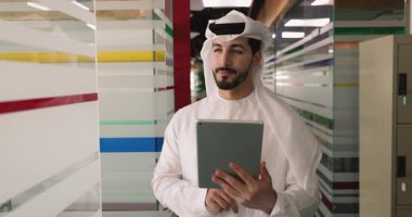 Geleneksel beyaz kandura gibi giyinmiş Cezayirli profesyonel işadamı finansal verileri inceliyor, raporları okuyor veya modern ofiste dijital tablet kullanarak iş operasyonlarını yönetiyor.