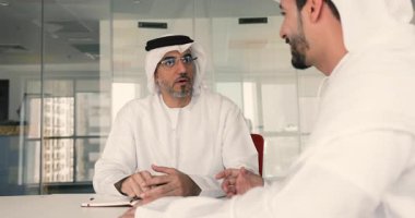 Geleneksel beyaz tobe giymiş orta doğulu yetişkin işadamı, konferans masasında oturan şirket müşterisiyle resmi bir toplantı yapıyor. İş iletişimi, müzakereler, sözleşme tartışması