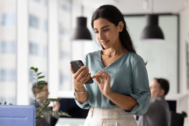 Genç 30 'lu yaşlarda iş yerinde akıllı telefon kullanan, mesajları kontrol eden, e-postaları okuyan, işle ilgili bilgileri inceleyen, iş saatlerinde bağlı kalan, dijital iletişimle meşgul olan bir kadın.