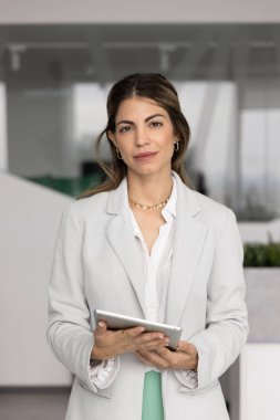 Elinde dijital tablet bulunan ciddi iş kadını portresi kameraya bakıyor. Güven, profesyonellik ve otorite yayıyor. Yeni yenilikçi yapay zeka iş platformu kullanarak internet üzerinden iş akışından uzaklaşıyor.