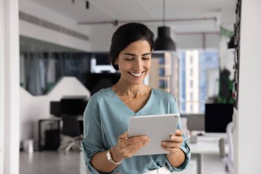 Gülümseyen Latin iş kadını tablet ekrana bakıyor, e-posta ile işle ilgili haberleri okuyor, raporları veya belgeleri inceliyor, dijital içeriği izliyor, modern aygıt kullanarak odaklanmış iş akışına katılıyor